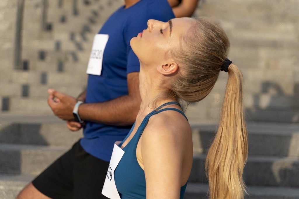 Läuferin schließt kurz vor dem Start die Augen und fokussiert ihre Atmung – sie nutzt Entspannungstechniken im Sport, um im Hier und Jetzt zu leben und Ruhe vor dem Wettkampf zu finden.