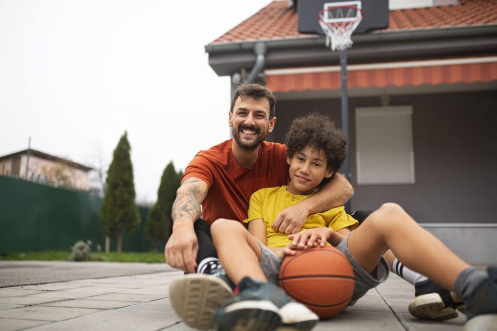 Vater sitzt mit seinem Kind und einem Basketball vor dem Haus – Symbol dafür, wie Sportpsychologie für Eltern ihre Kinder im Sport einfühlsam und stärkend begleiten kann.