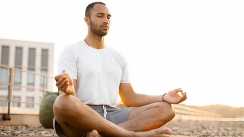 Sportler sitzt meditierend im Schneidersitz im Freien, nutzt Entspannungstechniken im Sport, um zur Ruhe zu kommen und im Hier und Jetzt zu leben.