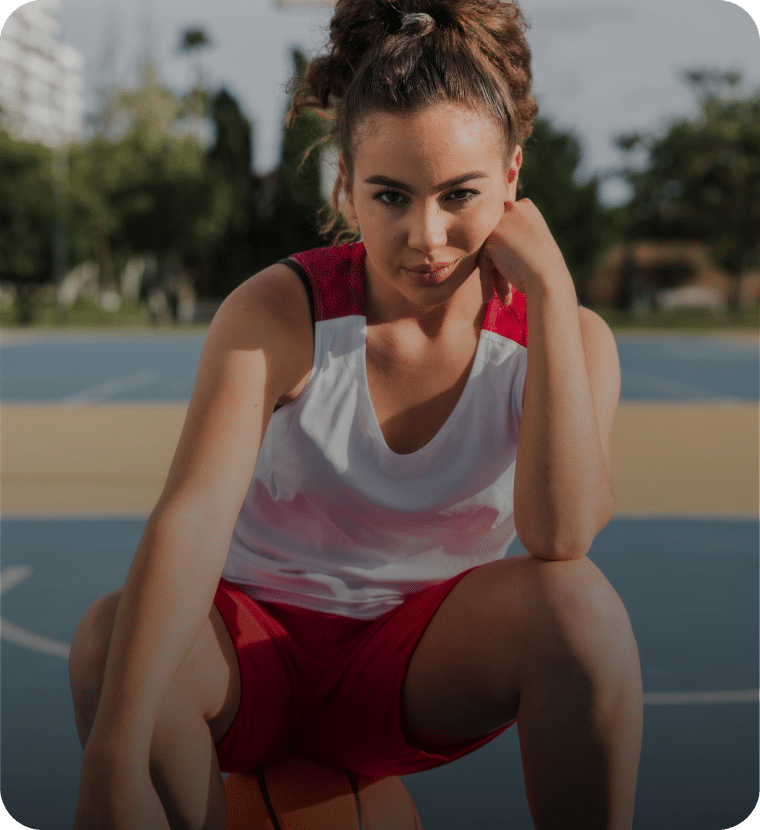 Fokussierte Basketballspielerin sitzt nachdenklich auf dem Ball auf dem Court – Symbol für mentale Wettkampfvorbereitung und gezieltes Mentaltraining vor Wettkampf.