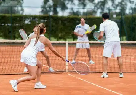 Tennis-Doppel beim Spiel auf Sandplatz, unterstützt von einem Mentaltrainer Tennis, der Teamfokus, Kommunikation und mentale Stärke fördert.